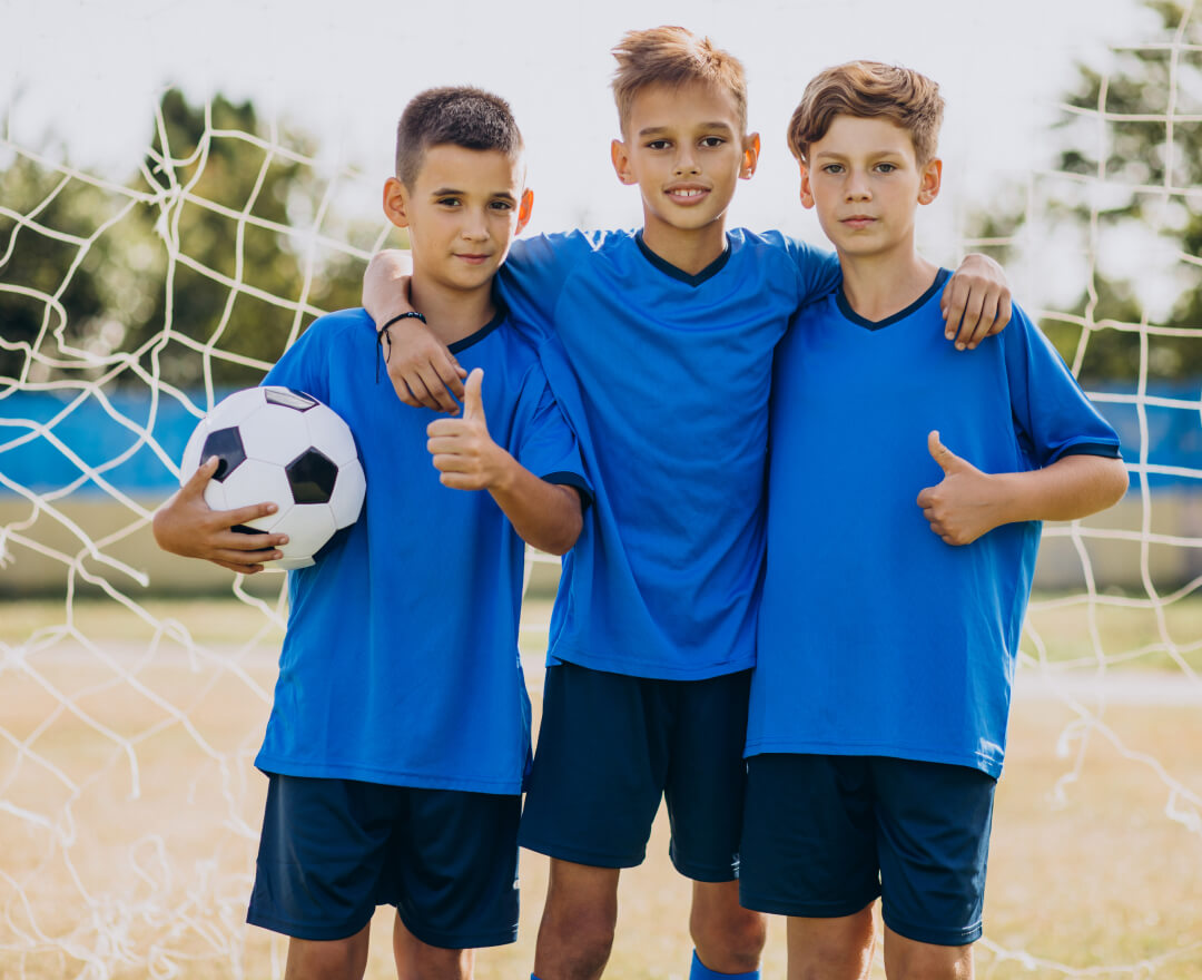 drei laechelnde jungs mit fussball vorm tor in der tossakan sportakademie